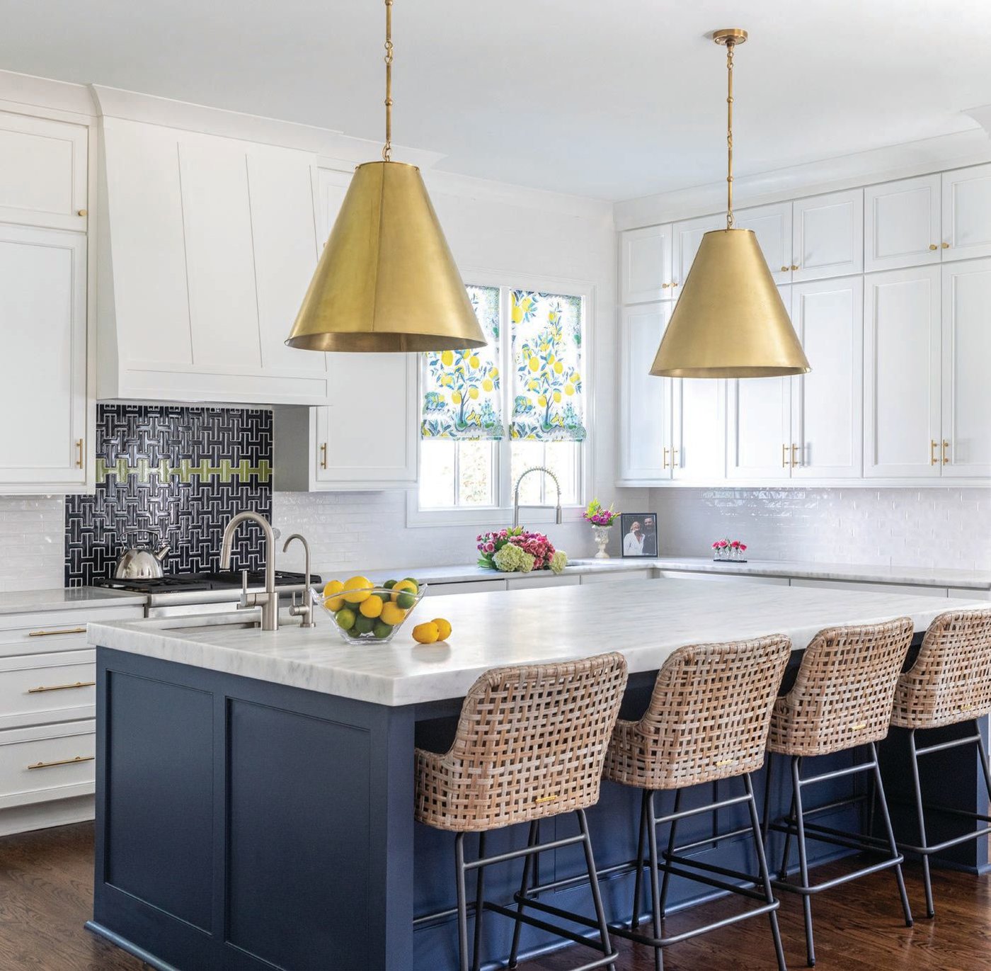 A kitchen island in Sherwin-Williams’ Naval paint with rattan-style chairs from Ballard Designs and oversized golden pendant lights by Circa Lighting. Photographed by Heidi Harris Photography
