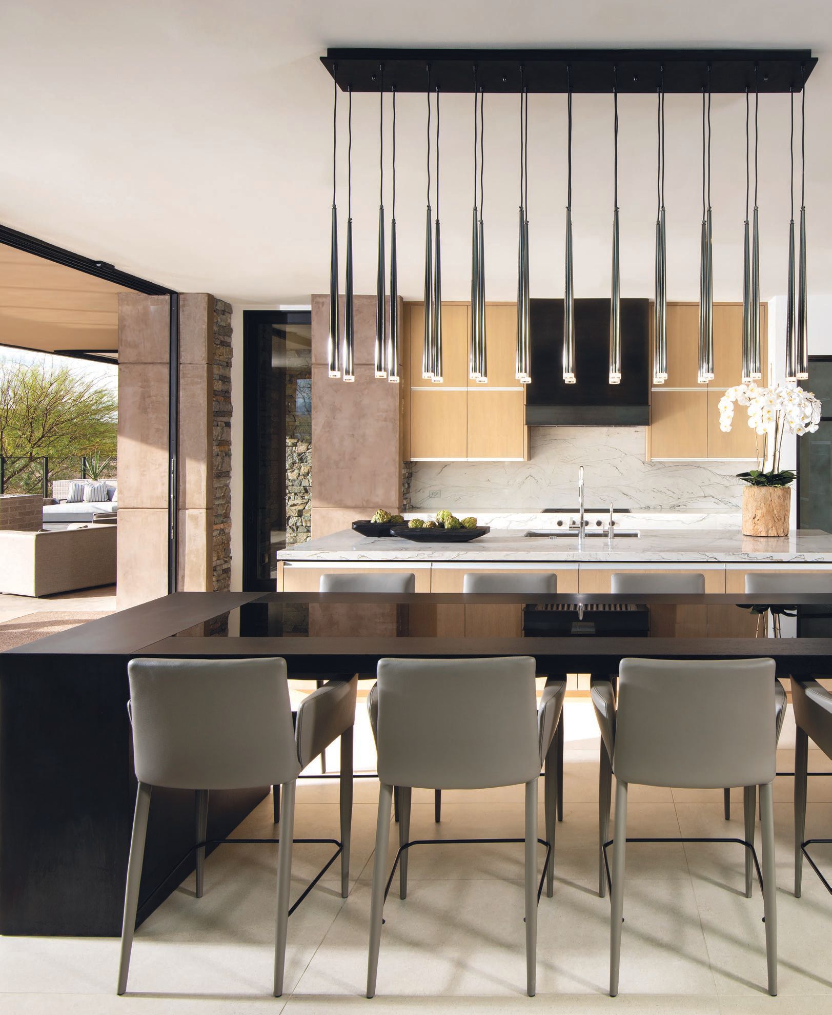 “One of our favorite pieces in this kitchen besides the timeless material palette is the custom-made dining table,” says Ownby. “This table is made of a triple-burnt live-edge wood slab that is channeled with smoke glass down the middle. A chandelier by Tech Lighting makes a major statement. PHOTO BY DINO TONN