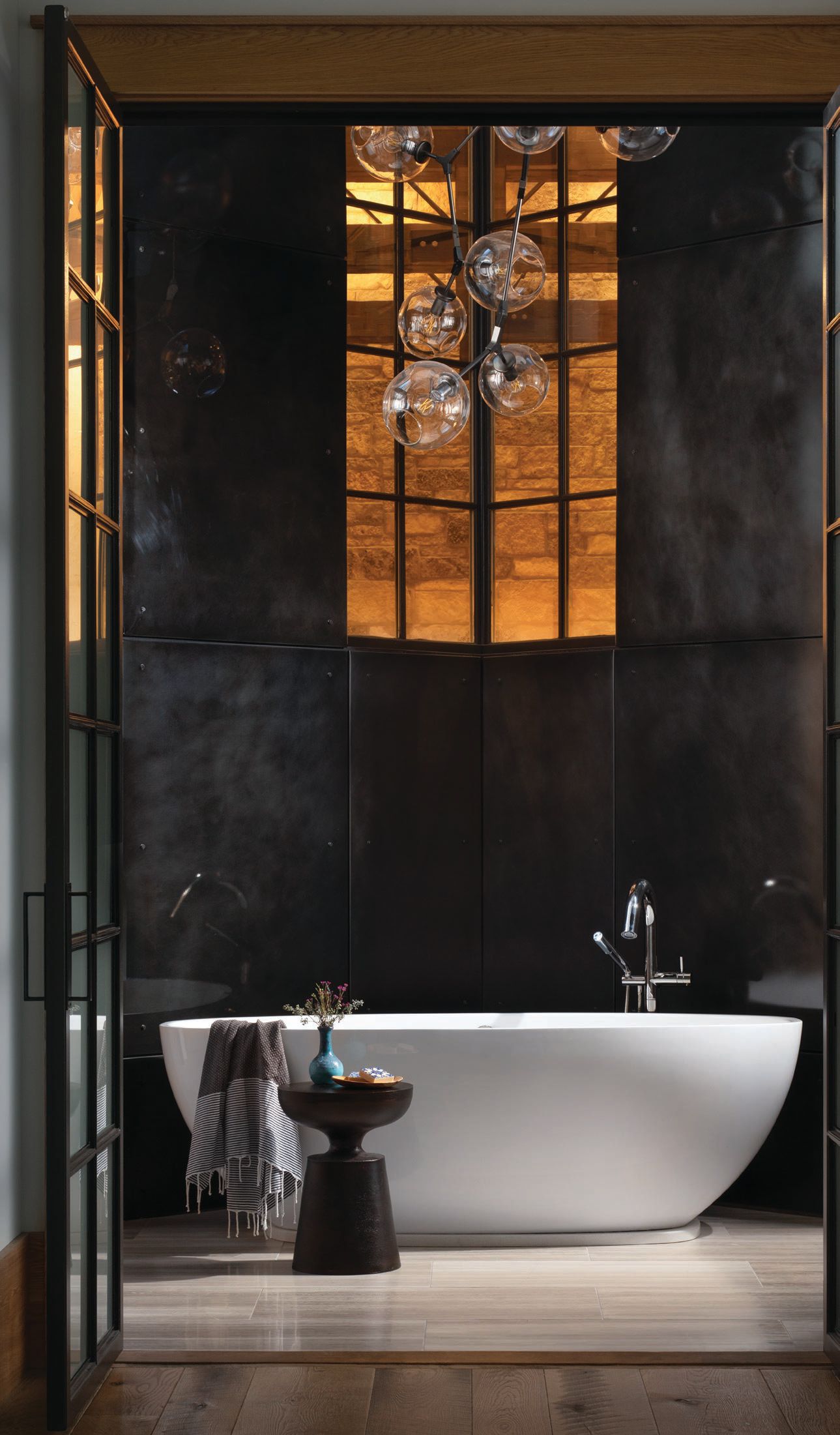 A free-standing Barcelona tub from Victoria   Albert with Riobel tub filler forms the centerpiece of the primary bathroom, which also features a striking vintage light fixture. Photographed by Ryan Hainey