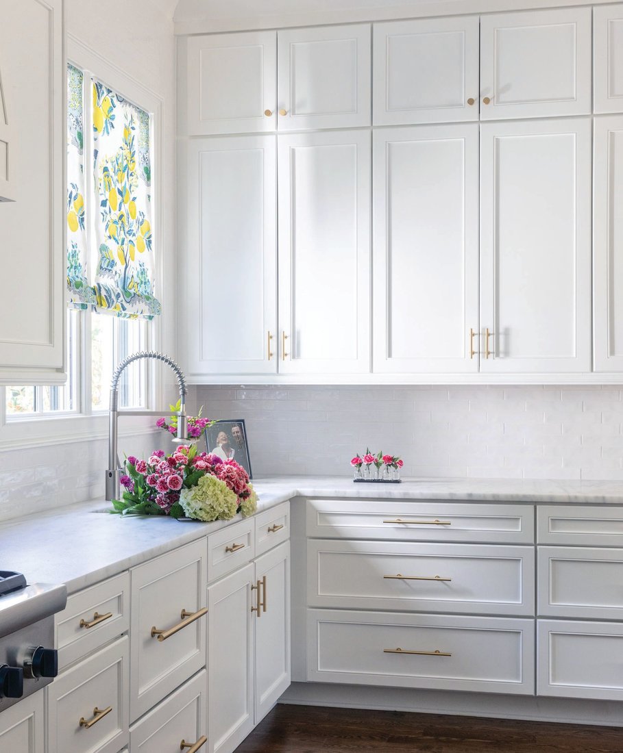 A corner of the kitchen features drapes by Schumacher in Citrus Garden pattern and Pool colorway offset by white cabinets with gold hardware. Photographed by Heidi Harris Photography