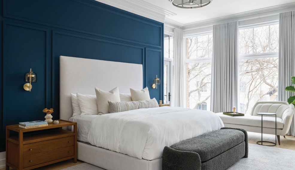 An eye-catching accent wall in Benjamin Moore’s Blue Note adds pop to the primary bedroom, which also features a chaise from Four Hands and window coverings by Blinds Gallery. Photographed by Dustin Halleck